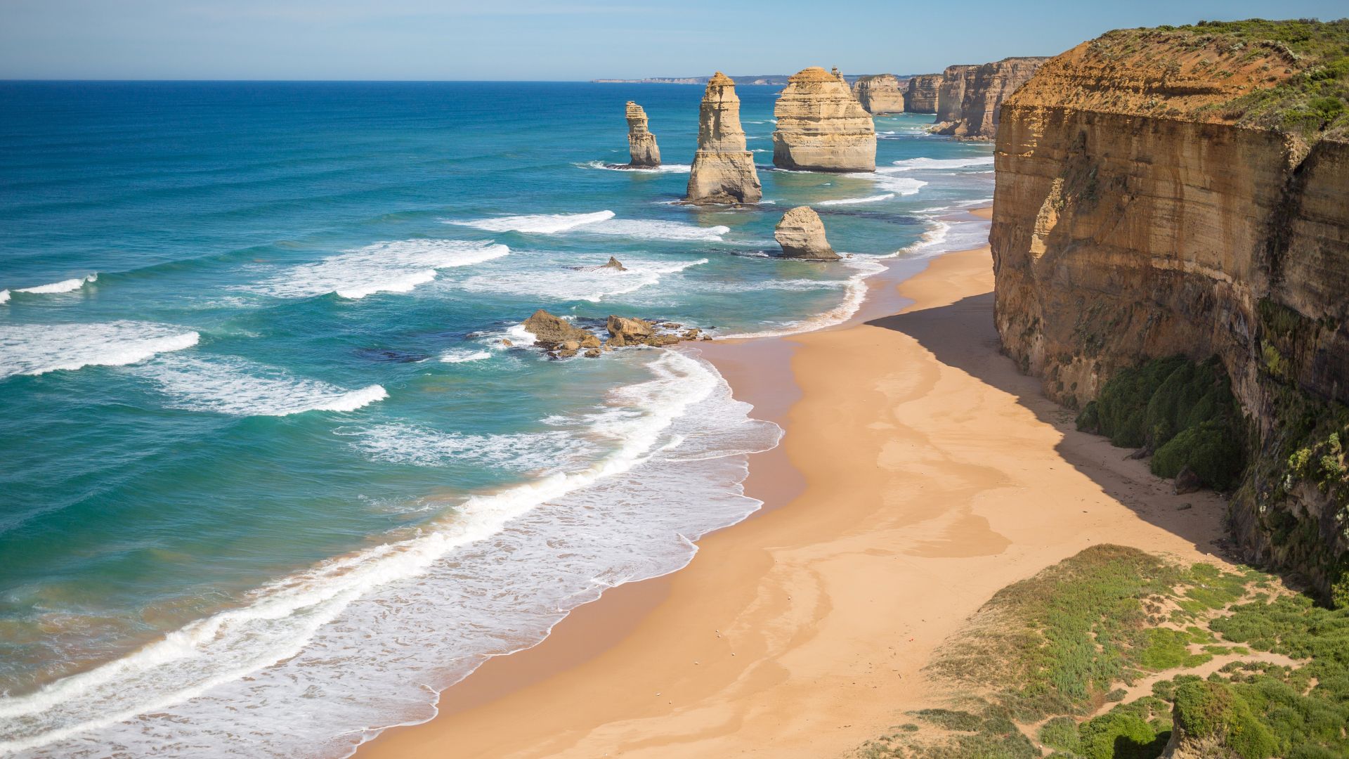 Turquoise ocean with limestone sea stacks, tall sandstone cliffs, and empty sandy beach.