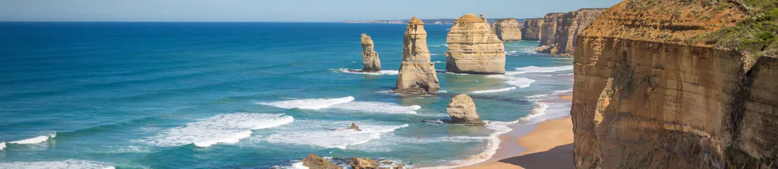 Turquoise ocean with limestone sea stacks, tall sandstone cliffs, and empty sandy beach.
