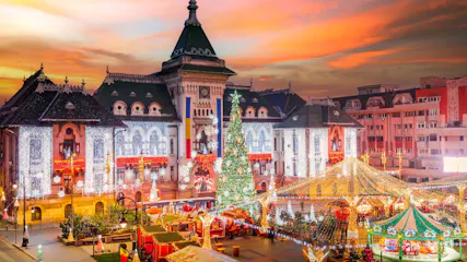 Historic building lit with Christmas lights beside a large tree and market stalls at sunset