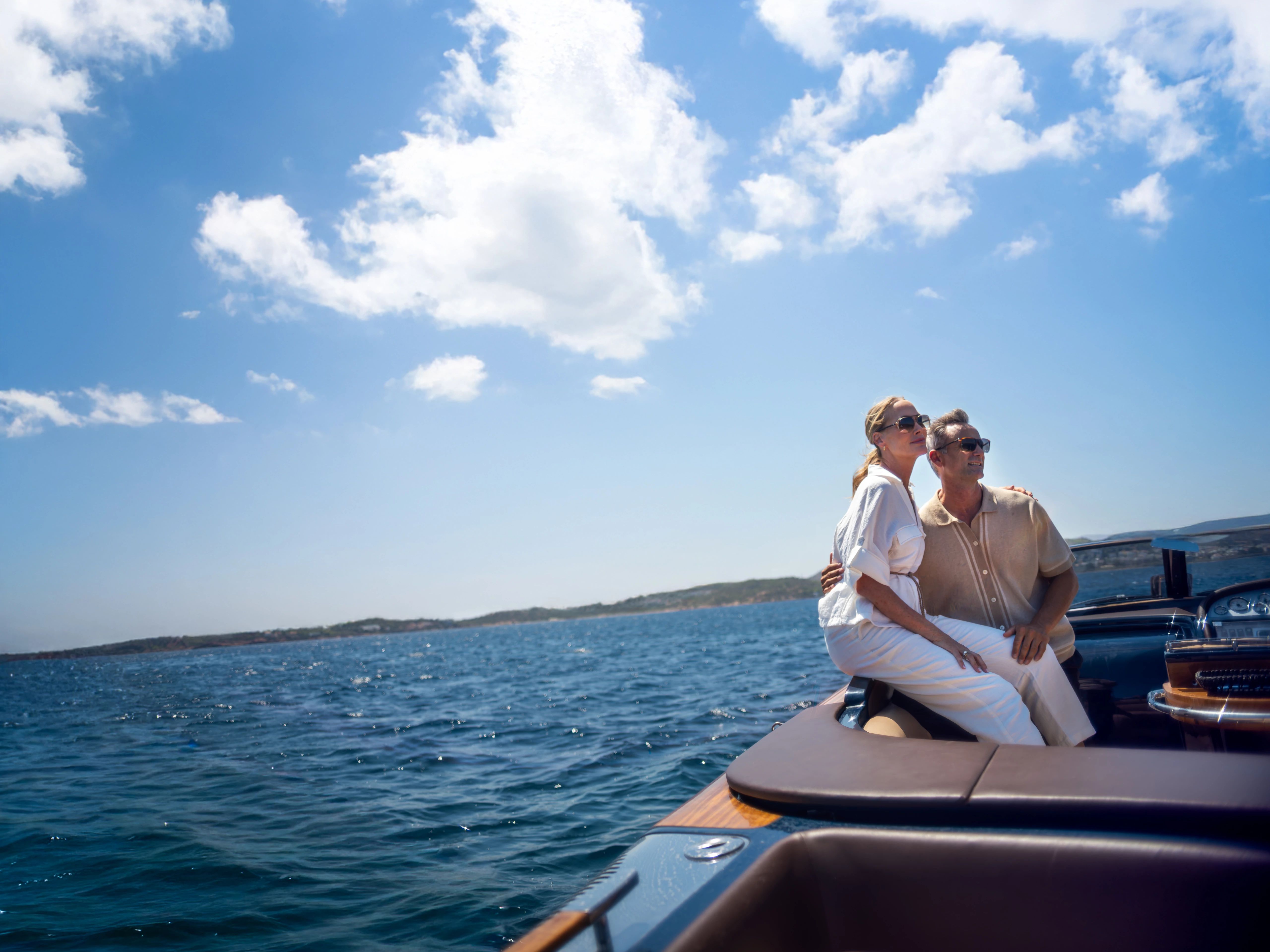 Couple on a boat's bow, arm around each other, wearing sunglasses, gazing at sea