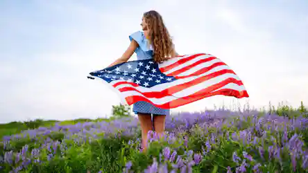 Woman with long curly hair in blue polka-dot dress in purple wildflowers holding American flag