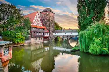 Half-timbered riverside house, stone tower and arched bridge over calm river at sunset