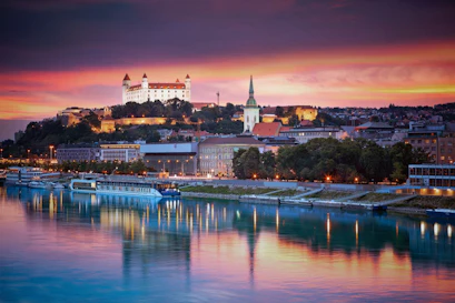 Bratislava Castle and spired cathedral above the Danube at sunset, boats reflected