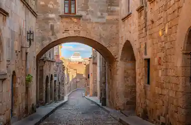 Narrow cobbled medieval street framed by stone arches and a distant cruise ship funnel