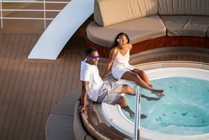 Couple laughing with feet in a yacht hot tub, relaxing on wooden deck near curved lounge