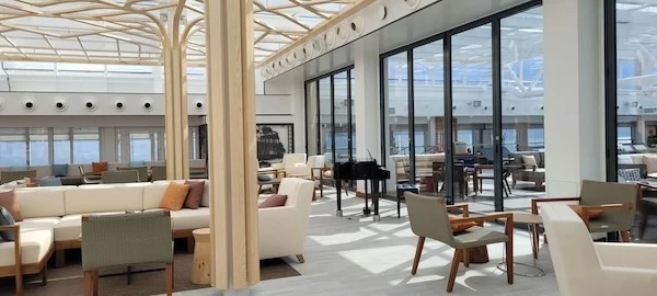Spacious modern lounge with sofas, armchairs, glass partitions, wooden columns, grand piano.