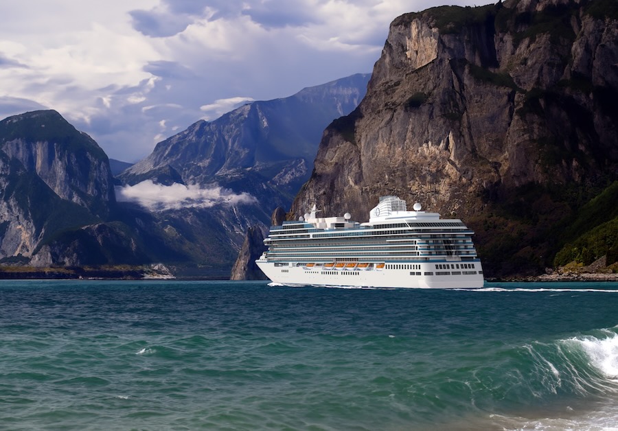 White cruise ship sailing through turquoise fjord with towering rocky cliffs and cloudy sky