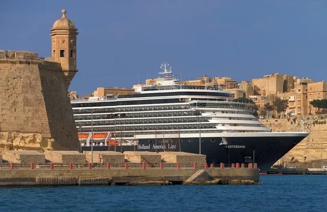 Holland America cruise ship docked beside a stone bastion and watchtower in a Mediterranean harbor
