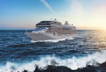 White luxury cruise ship named 'Seven Seas Grandeur' sailing at sunset across choppy ocean