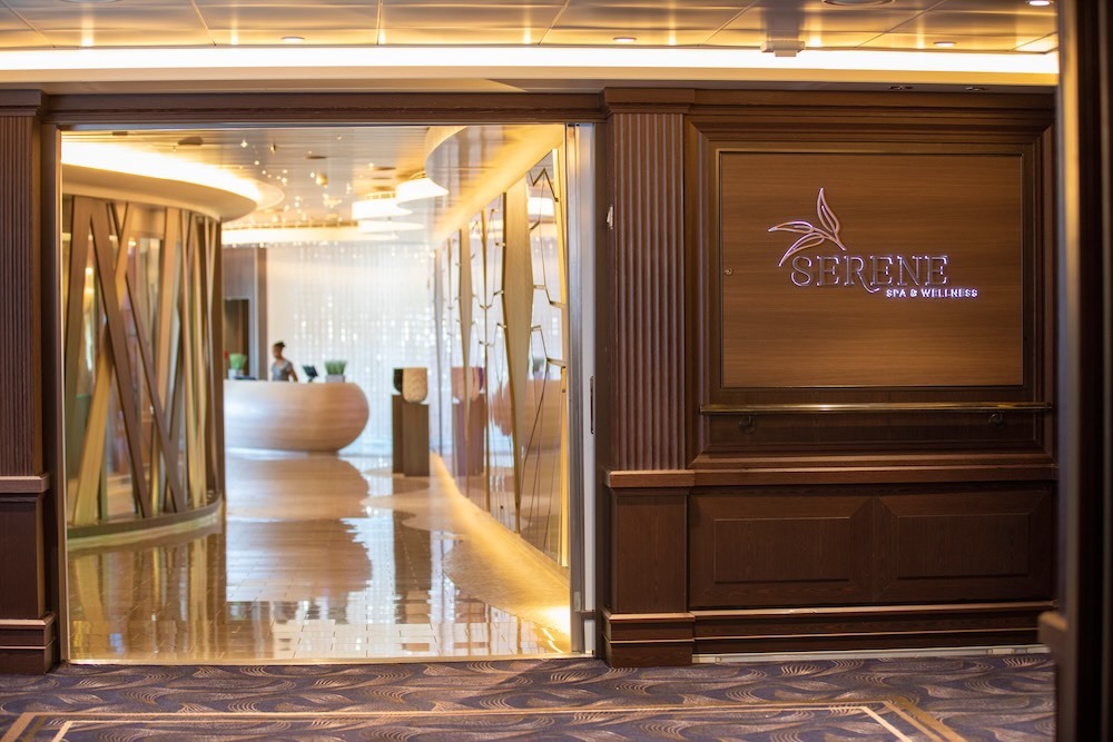 Entrance to Serene Spa & Wellness with wooden sign, open lobby, curved reception desk and staff.