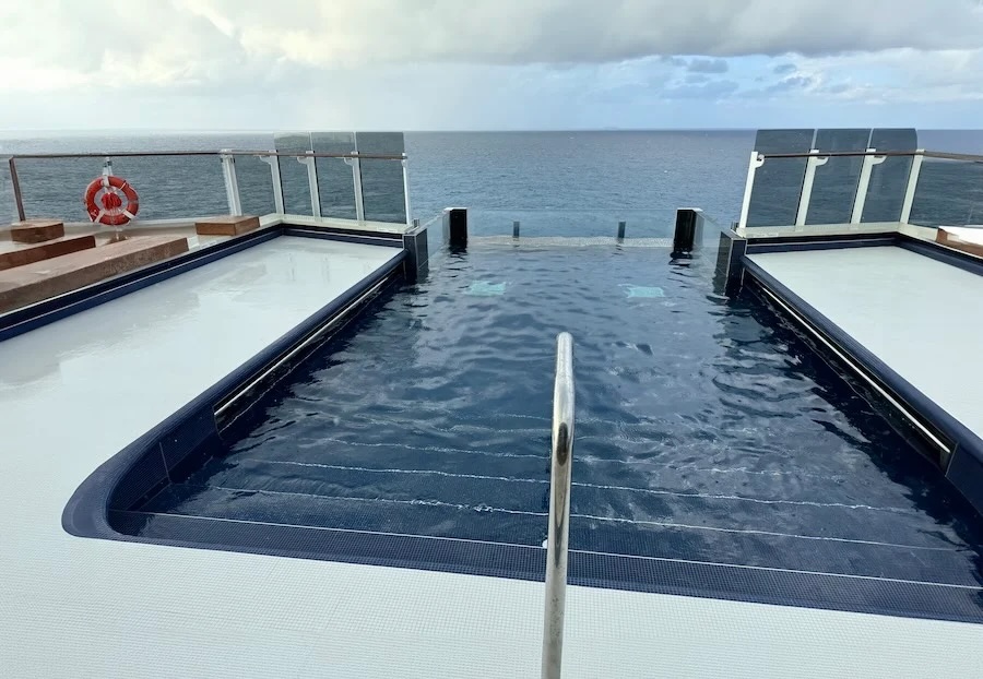 Infinity pool with central handrail on a ship deck overlooking the open ocean and cloudy sky