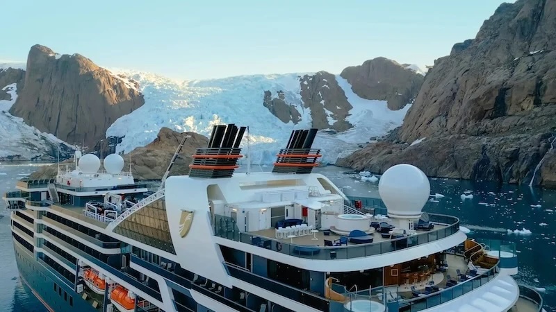 Luxury cruise ship amid floating ice in a fjord beneath a blue glacier and rocky cliffs