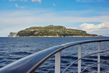 Ship railing foreground with blue sea and a distant green island under a bright sky