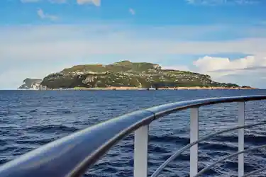 Ship railing foreground with blue sea and a distant green island under a bright sky