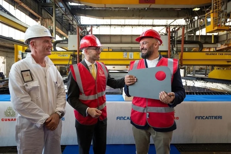 Three men in hard hats and red safety vests at Fincantieri shipyard, smiling and holding plaque