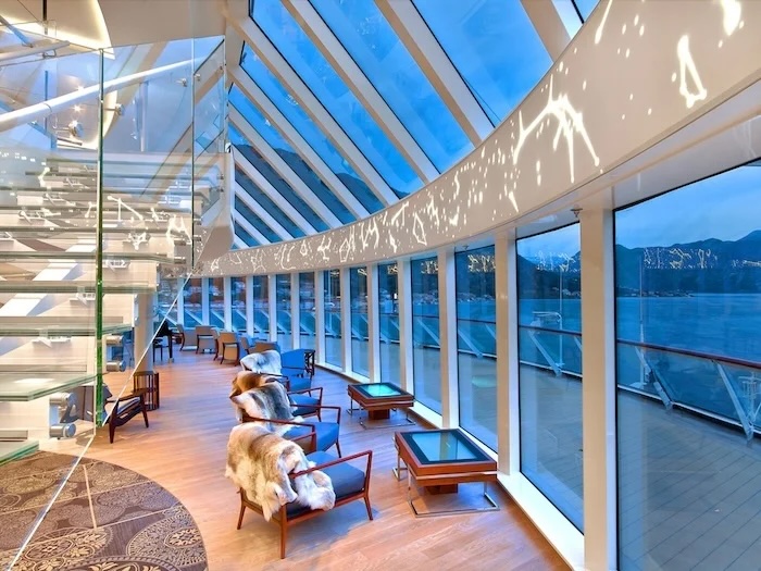 Glass-walled cruise ship observation lounge with armchairs draped in fur and ocean views