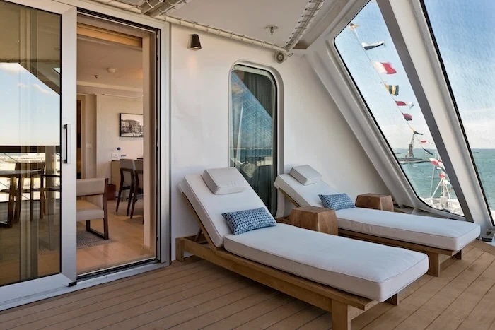 Private cruise balcony with two white-cushioned loungers, wooden side tables and ocean view