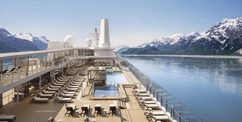 Cruise ship sun deck with pool and lounge chairs beside glass railings facing snow-capped mountains