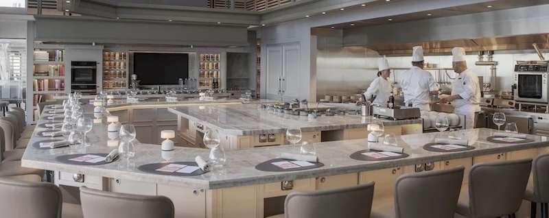 U-shaped demonstration kitchen with marble counters, set places, and three chefs cooking