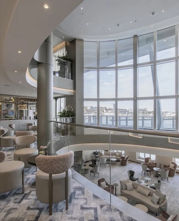 Two-level lounge with floor-to-ceiling curved windows, waterfront view, clustered neutral seating