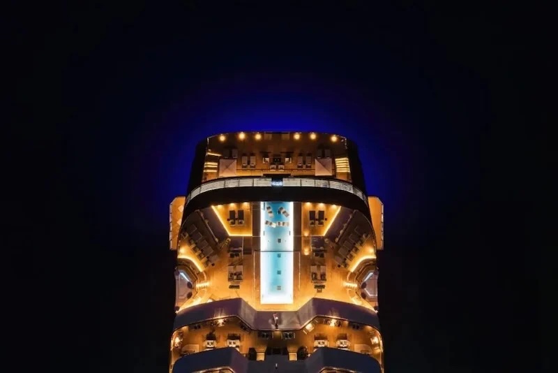 Aerial night view of illuminated cruise ship deck with central rectangular pool and lounge chairs