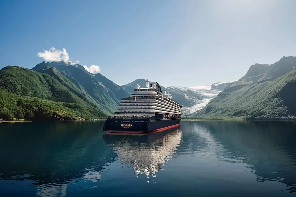 Large cruise ship "Explora" centered in a calm fjord with glacier-backed green mountains