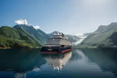 Large cruise ship "Explora" centered in a calm fjord with glacier-backed green mountains