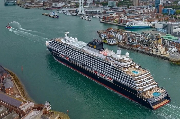 Aerial view of a large multi-deck cruise ship with pools entering a city harbor near shore