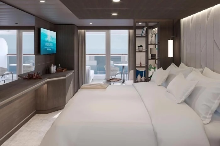 Luxurious cruise ship stateroom with king bed, bedside shelves, TV and balcony seating.
