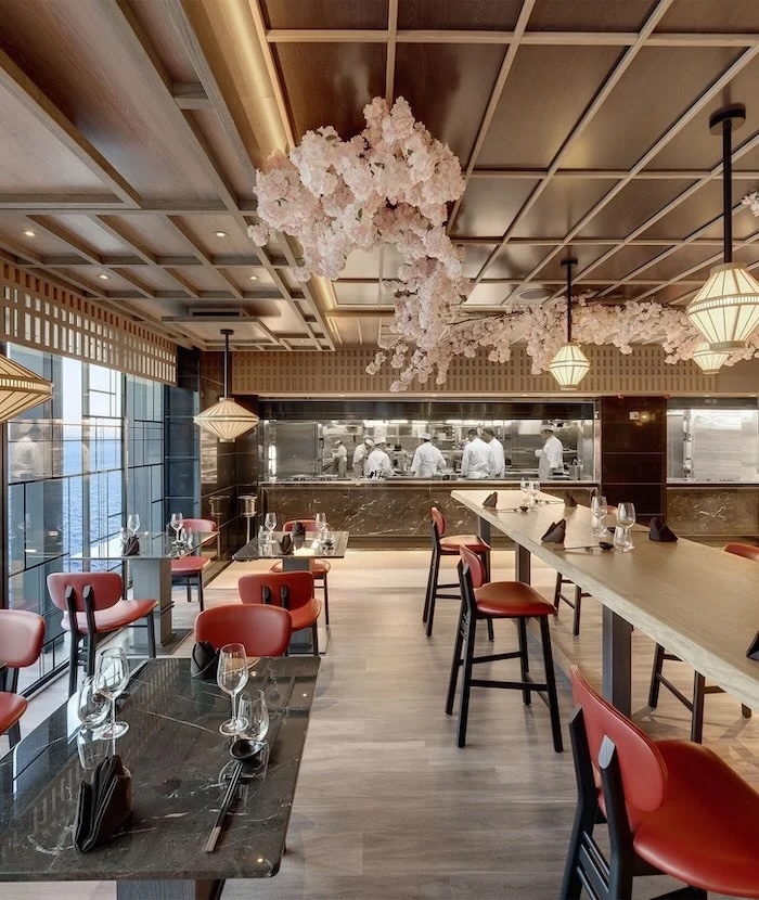 Upscale restaurant interior with pink cherry-blossom ceiling, open kitchen with chefs, red chairs