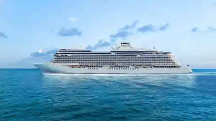 Large white multi-deck luxury cruise ship sailing on calm blue ocean beneath pale sky