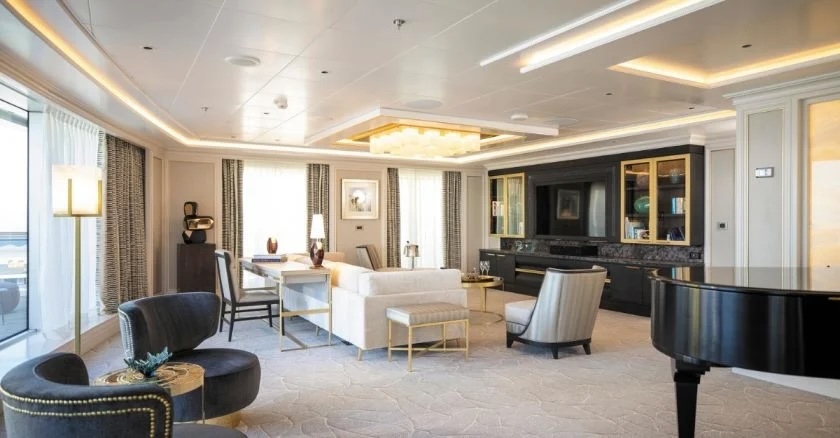 Luxury suite living room with white sectional sofa, armchairs, grand piano and ocean-view balcony