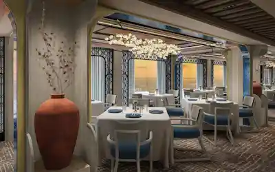 Upscale ocean-view dining room with white-tablecloth tables, blue chairs, terracotta vase