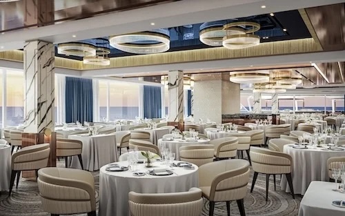 Cruise ship dining room with round white tables, beige chairs, ring chandeliers, ocean windows.
