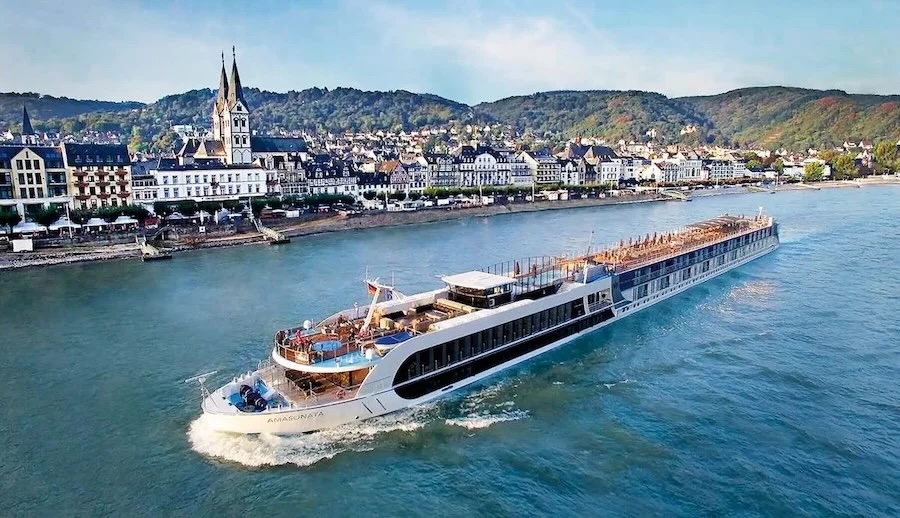 River cruise ship passing a European riverside town with church spire and tree-covered hills