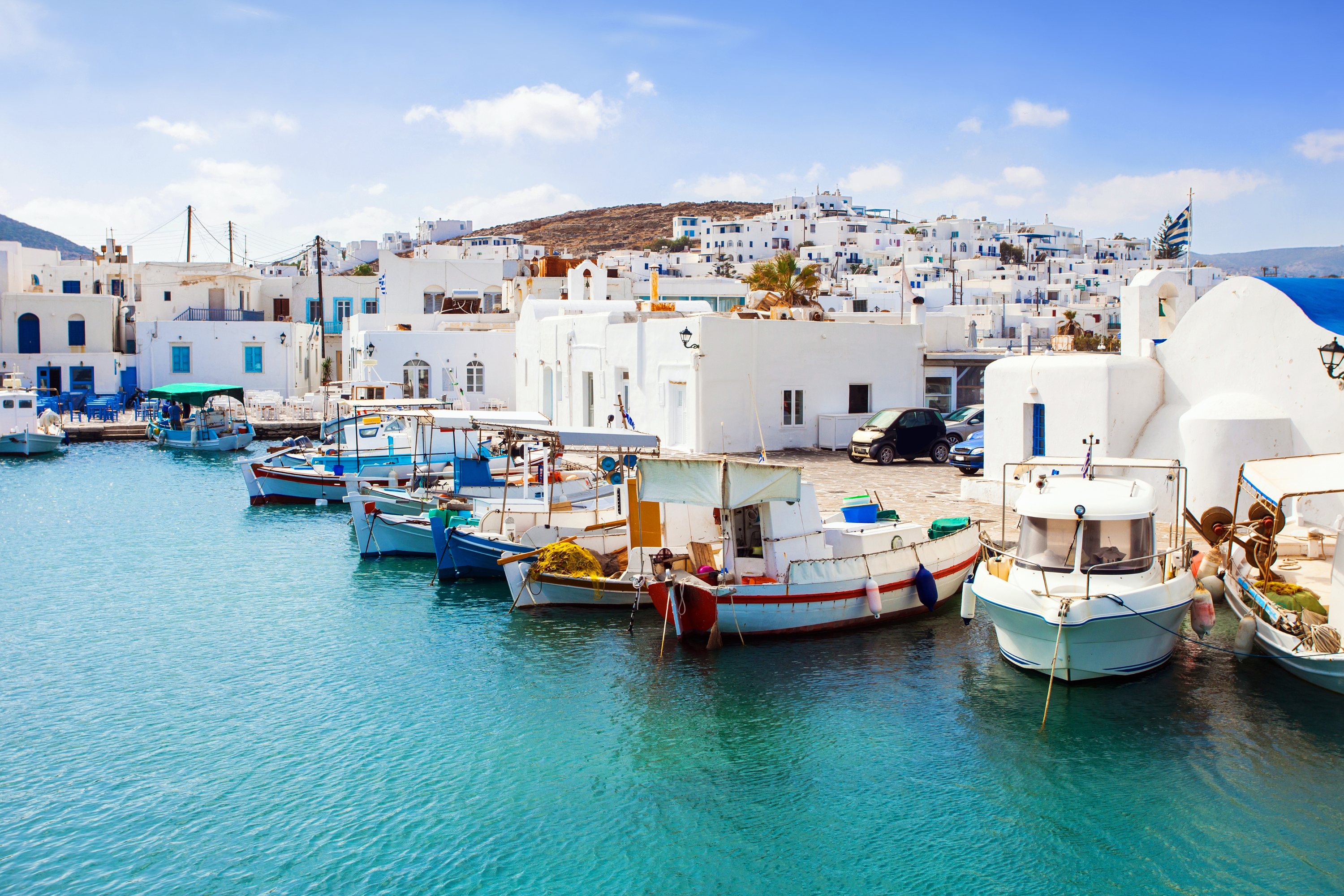 Fishing boats moored in turquoise harbor before whitewashed Greek island village and a Greek flag