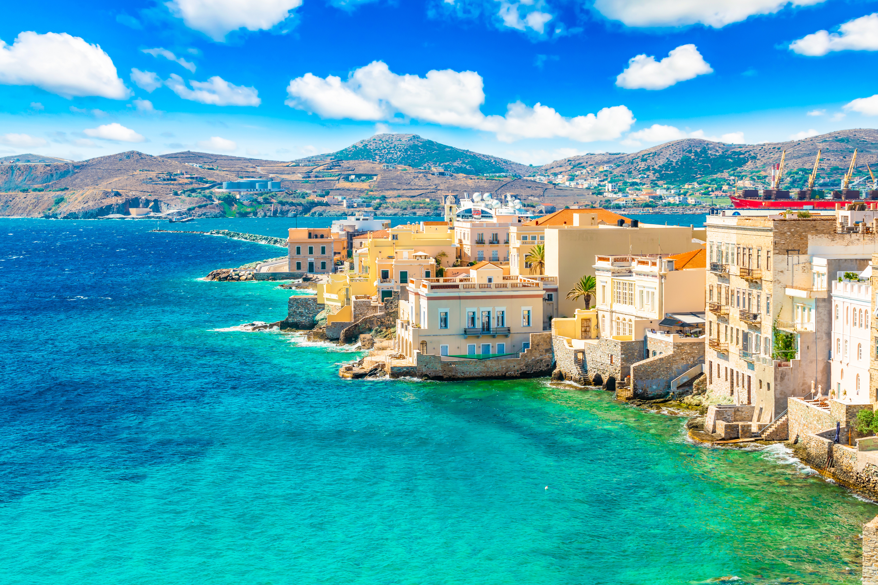 Mediterranean harbor town with pastel waterfront buildings, rocky shore, turquoise sea