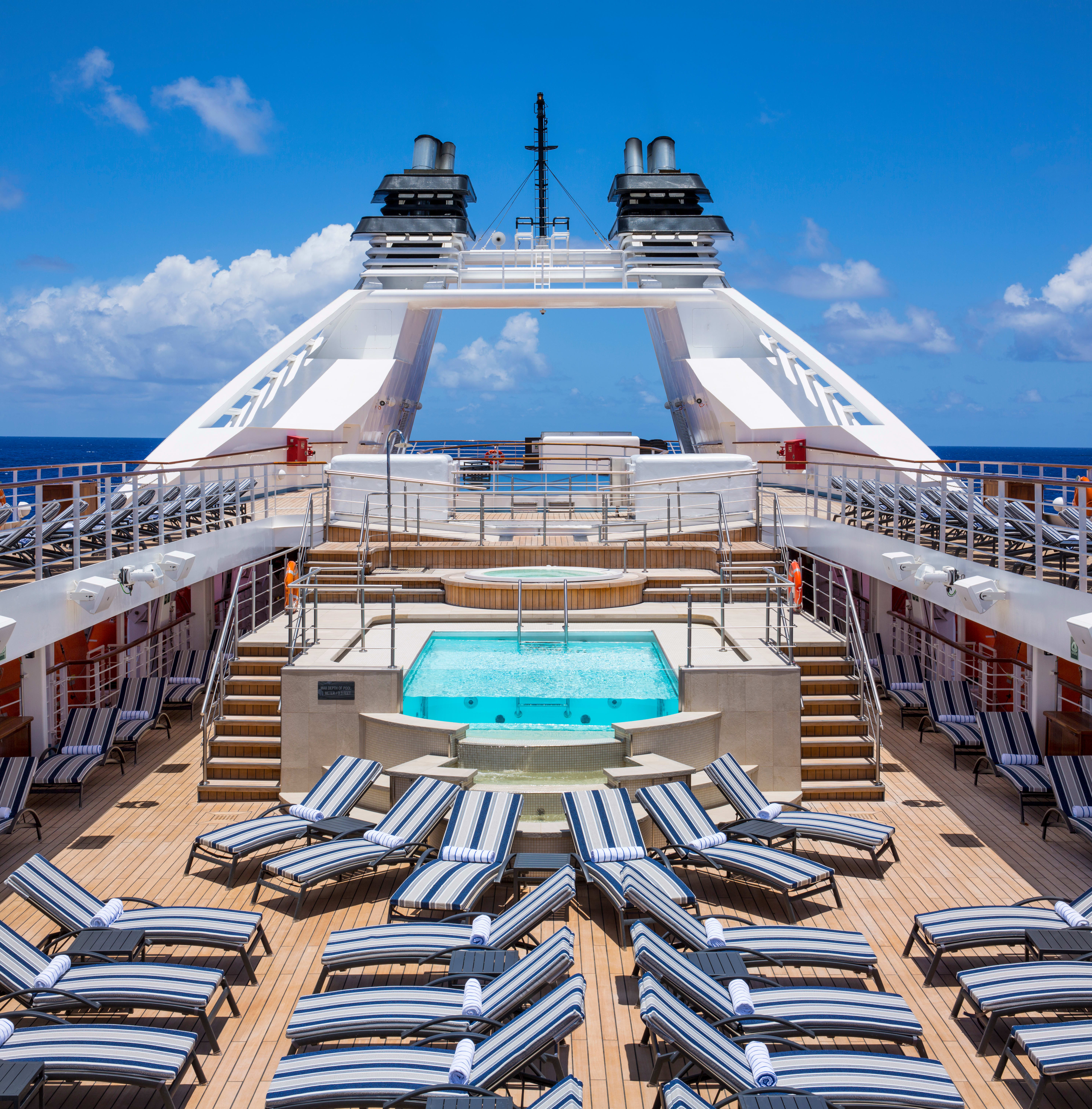 Cruise ship sun deck with blue-striped loungers, central pool and twin funnels
