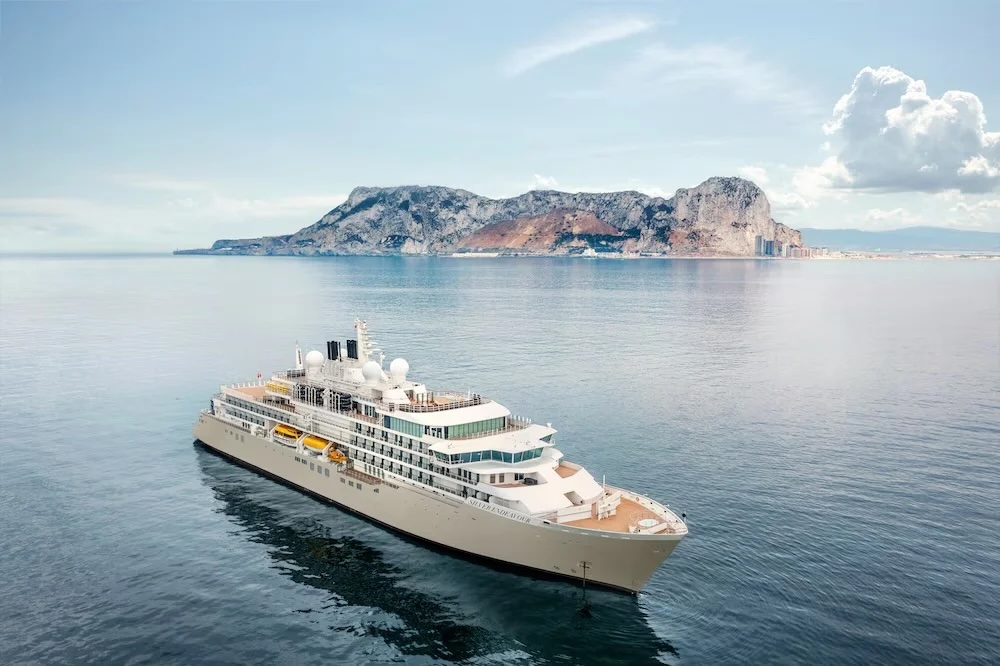 White luxury cruise ship cruising near a rocky coastal island under pale blue sky