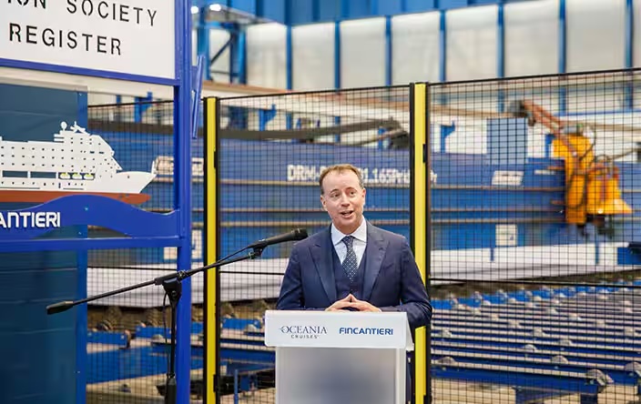 Man in suit speaking at Oceania Cruises and Fincantieri podium in shipyard