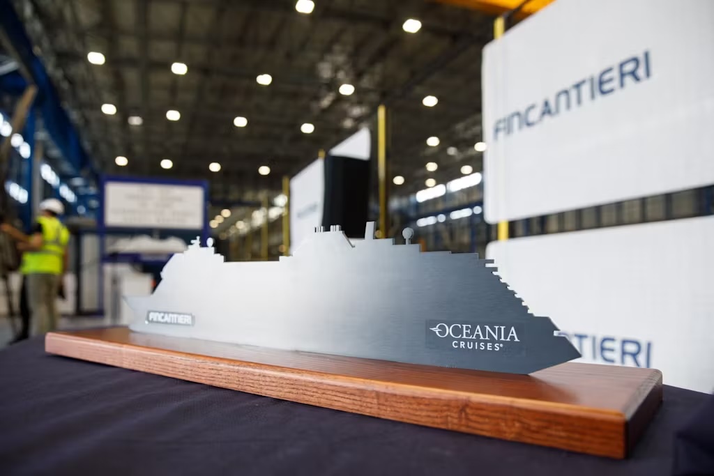 Metal ship silhouette on wooden base reading "Oceania Cruises" with Fincantieri signage in background
