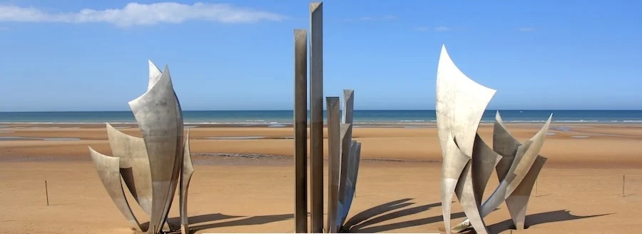 Stainless-steel sail-shaped memorial sculptures on expansive sandy beach overlooking the sea