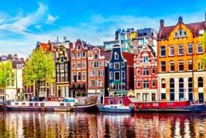 Canal with moored boats and reflections before a row of colorful gabled Amsterdam houses