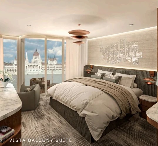 Balcony suite with king bed, seating, desk and balcony overlooking parliament across river