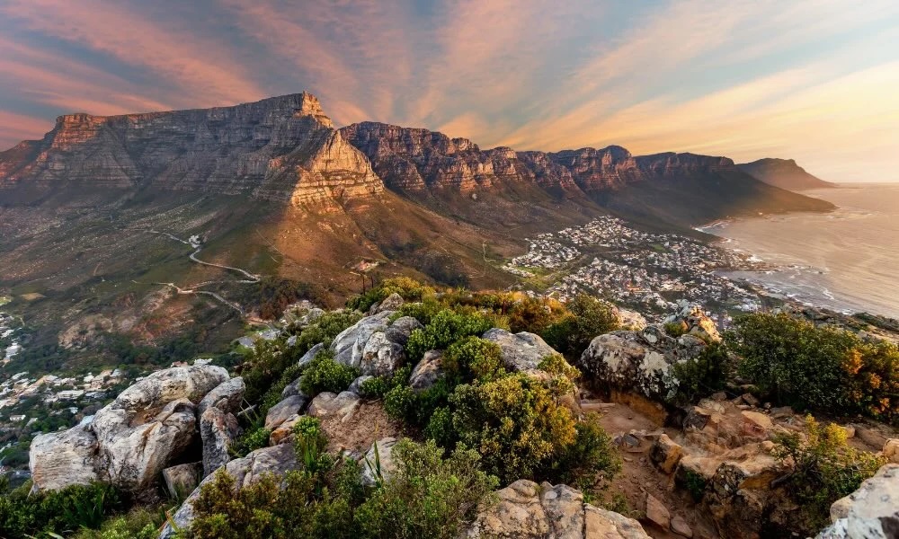 Sunset view from rocky foreground over Table Mountain and Twelve Apostles above Cape Town coast