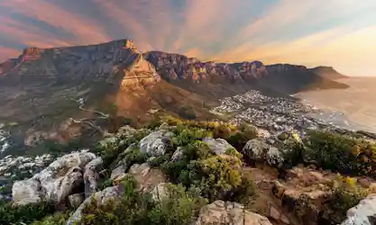 Sunset view from rocky foreground over Table Mountain and Twelve Apostles above Cape Town coast
