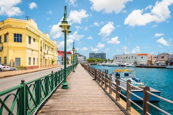 Harbor boardwalk with green lampposts, yellow colonial building left, boats docked right.