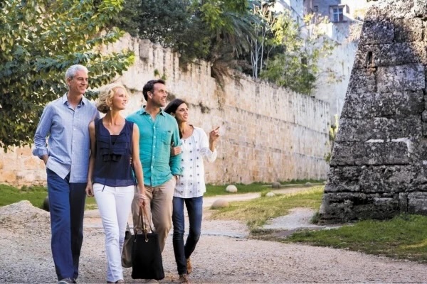Four adults strolling and sightseeing along a gravel path beside an ancient stone wall and ruin