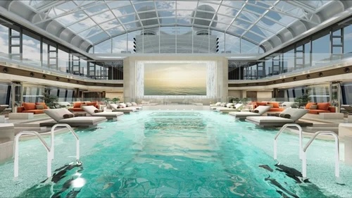 Glass-domed indoor pool with turquoise water, chaise lounges, upper balconies, large screen