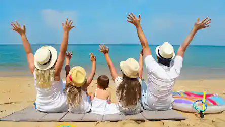 Parents and three children on a beach mat facing the ocean, arms raised, wearing sun hats